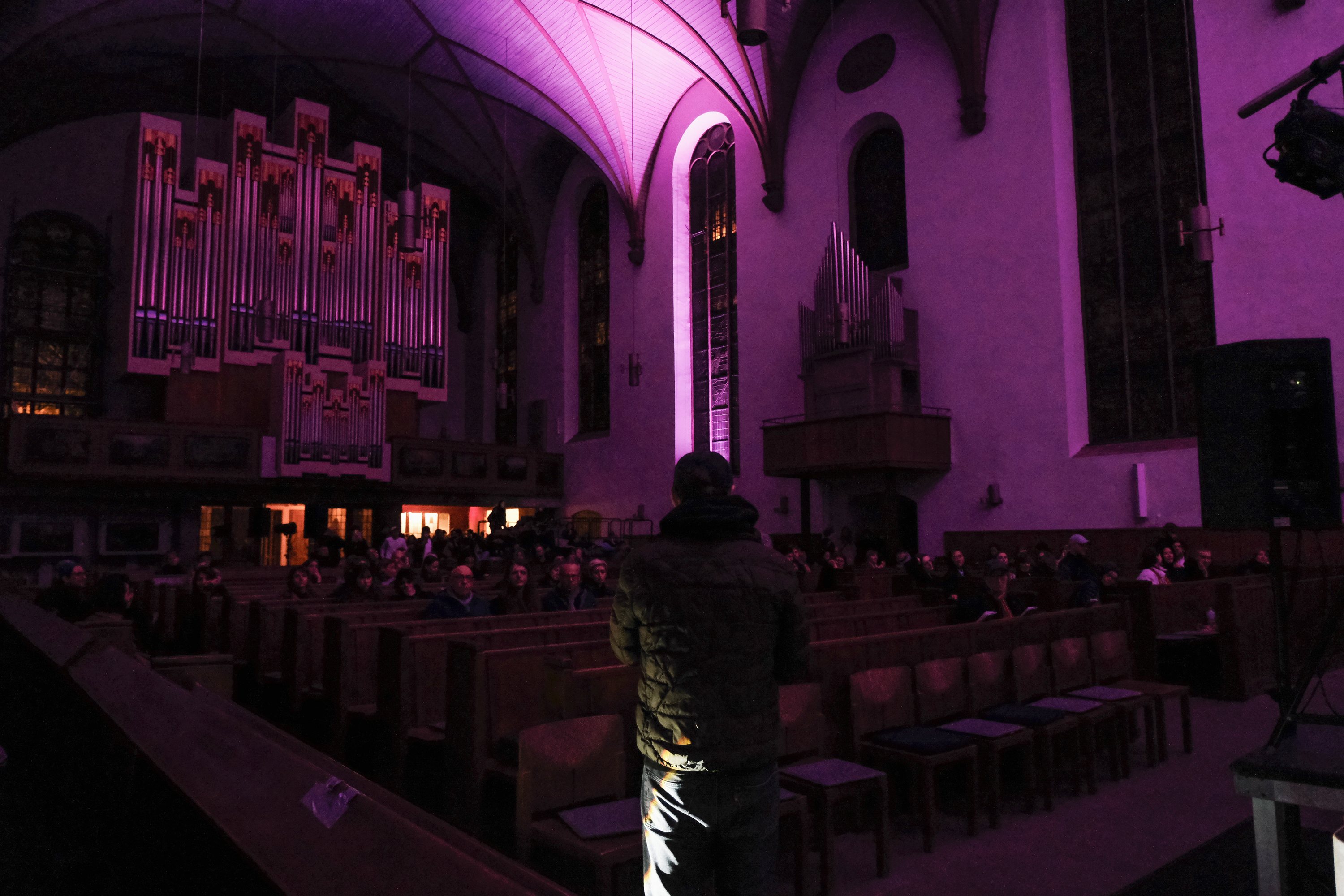 Das Kirchenschiff mit der Orgel im violetten Licht, Publikum in den Bänken