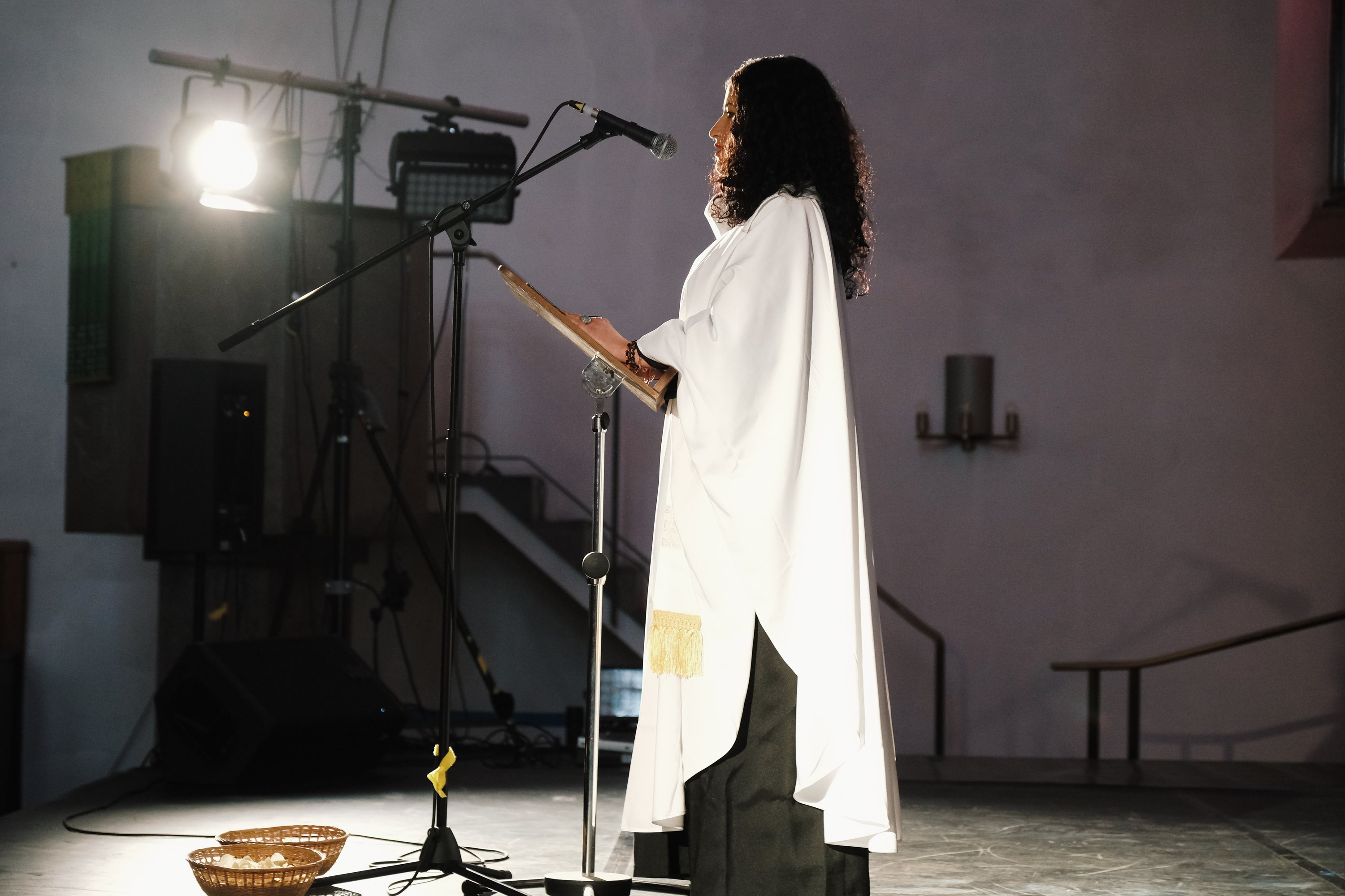 Performer*in im weißen Gewand am Mikrofon im Scheinwerferlicht